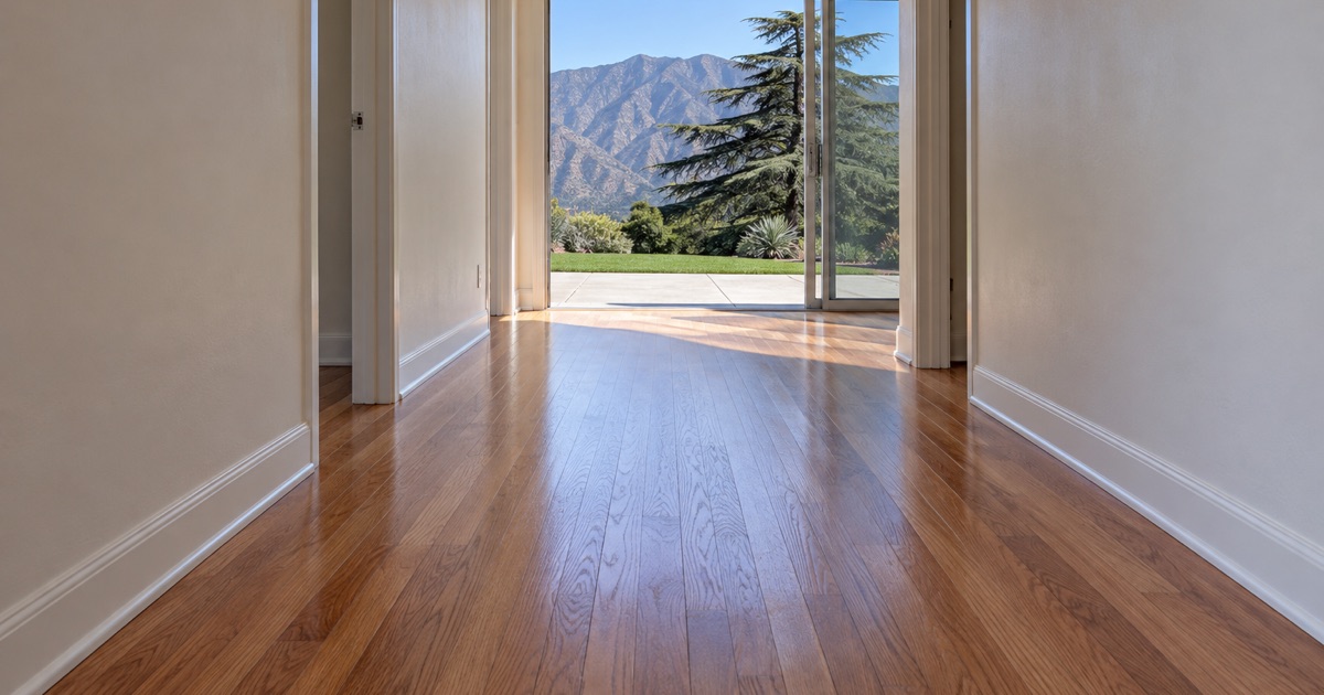 Finished oak floor running down the gallery hall of a 1950s ranch house in Arcadia to an open sliding door and the mountains beyond.